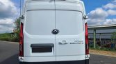Rear view of a white Maxus eDeliver 9 van with dual rear doors and centered logo, parked near an industrial area.