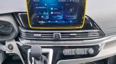 Center console of a car with a large infotainment touchscreen framed in yellow, gear shifter in front, and climate controls below the screen.