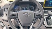 Close-up of a car steering wheel with cruise and multimedia controls, a digital instrument cluster, and a gear selector visible to the right inside a modern vehicle cabin