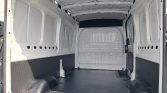 Empty white cargo van interior with a black rubber floor and rounded wheel wells along the sides.