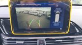 Car rearview camera display with colored guide lines (green/yellow/red) and a right-side parking-sensor graphic, plus the caution text “Please check surroundings for safety!”.