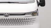 Front view of a white delivery truck: emblem centered on the grille, honeycomb-like perforated lower grille, and a sharp headlight to the right.