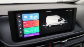 Infotainment touchscreen in a car showing colorful app tiles (CarPlay, Android Auto) and a white van diagram on the right side.