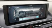 Large car dashboard touchscreen showing dual-zone climate control interface and temperature sliders; steering wheel visible in the background.