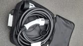 Coiled electric vehicle charging cable with a Type 2 connector tucked inside a black zipper case on pavement.