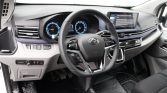Modern car interior showing steering wheel with mounted controls, digital instrument cluster, and a wide dashboard touchscreen.