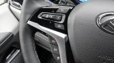 Close-up of a car steering wheel with left-side controls (OK, arrows) and cruise control buttons visible on the spoke, with part of the dashboard in view.