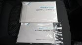 Two Maxus eDELIVER 7 booklets in plastic sleeves resting on a car seat, including a Warranty & Service Handbook labeled Maxus eDELIVER 7