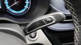 Automotic gear selector stalk showing R N D P with a Start/Engine Stop button below, in a car interior with a blue-lit speedometer in the background