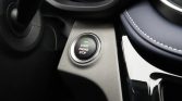 Car interior: circular push‑start button with green indicator light and text 'START ENGINE STOP' on textured beige panel near the gear area.
