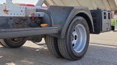 Close-up of a trailer wheel and gray fender on a utility trailer, showing exposed chassis and orange marker light/screw nearby.