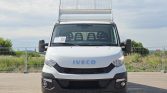 Front view of a white Iveco cargo van with a metal rooftop ladder rack in a parking lot.