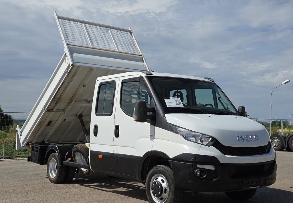 Front three-quarter view of a white Iveco tipper truck with its cargo bed raised for unloading on a sunny day.