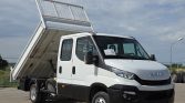 Front three-quarter view of a white Iveco tipper truck with its cargo bed raised for unloading on a sunny day.