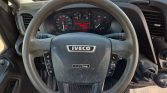 Steering wheel of an Iveco vehicle with dashboard gauges and a digital display behind it. The gear shifter is visible to the right.