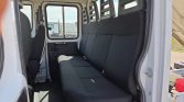Interior of a white cargo van with a long black bench seat along the side and visible seat belts, windowed side door in the background