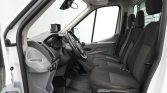 Front cabin of a white van showing the steering wheel, dashboard, and three fabric seats in the cargo area windowed door.
