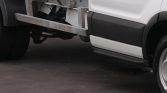 White van seen from the side with an exposed metal framework under the side and a metal side step/rail attached to the chassis.