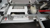 Metal framework of a truck’s rear chassis with a white plastic fluid reservoir and cables.