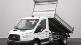 White Ford dump truck with its bed raised for dumping, orange warning beacon on roof, parked on a surface.