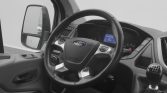 Interior of a Ford van: steering wheel with logo, gear shifter, and dashboard display visible in a grey-toned cabin