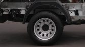 Truck wheel and chassis: silver steel rim with multiple holes, black fender above, exposed truck frame and components nearby.