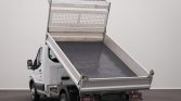 White utility pickup truck with its aluminum dump bed raised at a loading angle in a plain indoor space, ready to unload material.