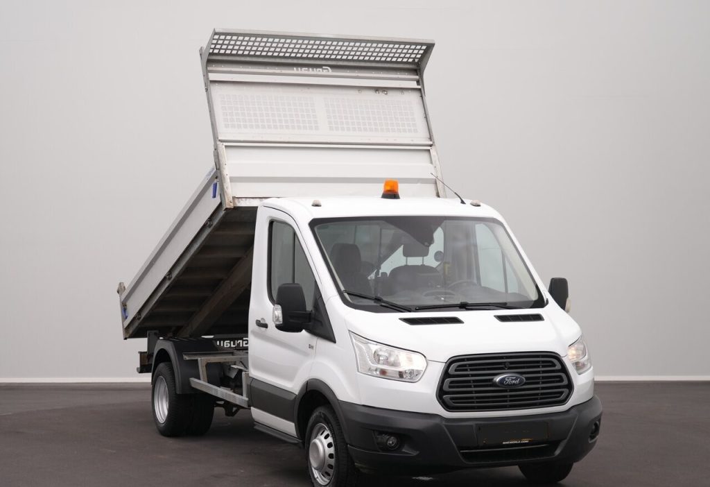 White Ford dump truck with its raised cargo bed, ready to unload gravel or dirt in a paved lot.
