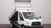 White Ford dump truck with its raised cargo bed, ready to unload gravel or dirt in a paved lot.