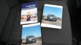 Three Ford vehicle manuals resting on a dark car seat: two show a blue Ford Transit van on the cover, and one features a woman with a child beside a car.