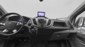 Front interior view of a Ford van showing steering wheel, manual gearshift, and central dashboard with an infotainment screen and air vents stretching across the dash.