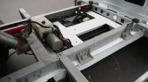 Exposed chassis of a white truck with a hydraulic motor, coolant reservoir, and wiring on a metal frame.