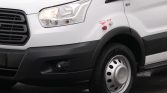 Front-left corner of a white delivery van showing headlight, grille, and front wheel with hubcap visible.
