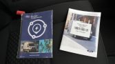 Two Ford manuals on a car seat: a blue 'BlueOval Charge Network' booklet and a white Transit owner’s guide with a barcode sticker on top.