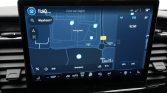 In-car navigation touchscreen showing a map with a blue location dot and route details in a car dashboard setting.