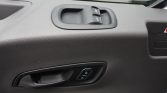 Driver-side front door interior with textured black panel, power window switches at the top, and a door handle with a lock button nearby. A partial hazard sign is visible on the right edge.