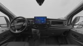 Front interior of a van showing a center touchscreen infotainment display, steering wheel, and driver-side dashboard components.