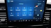 In-car touchscreen showing the 'Instellingen' settings menu with tiles: Radio, Telefoonlijst, Navigatie, Geluid, Voertuig, Klok, Algemeen, Display; map on the right side.