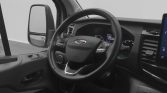 Driver's cockpit view featuring a Ford steering wheel, dashboard gauges, and side mirror in a van interior.