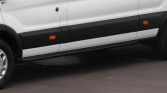 Side view of a white commercial van with black lower panels and orange side marker lights on the doors and paneling.