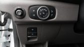 Close-up of a car dashboard: circular light control dial with surrounding buttons on a textured black panel, plus a small round knob on the left.
