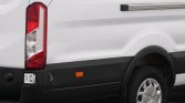 Rear side of a white cargo van with a red taillight, black bumper, and a visible wheel.