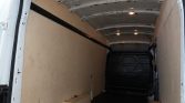 Interior of an empty cargo van with plywood side walls and ceiling lights visible ahead