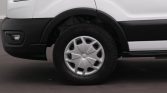 Front left wheel of a white van, showing the tire and silver hubcap with black fender and bumper nearby