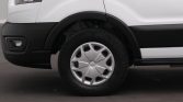 Close-up of a white van's front left wheel, showing the tire, silver hubcap, and wheel well.