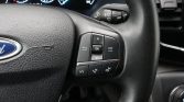 Close-up of a Ford steering wheel with left-hand control pad (OK, arrows, Menu) and phone/volume buttons.