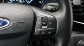 Close-up of Ford steering wheel controls on the right, including OK button and directional pad, with instrument cluster in background.