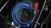 Coiled blue electric charging cable stored in a car trunk with connectors and clamps visible