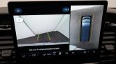 Car infotainment screen showing rearview camera feed (left) with guiding lines and a top-down parking view (right) to assist reversing in a garage.