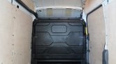 Interior view of an empty cargo van with wooden side panels and a black bulkhead at the rear, ceiling light on, looking toward the cab.
